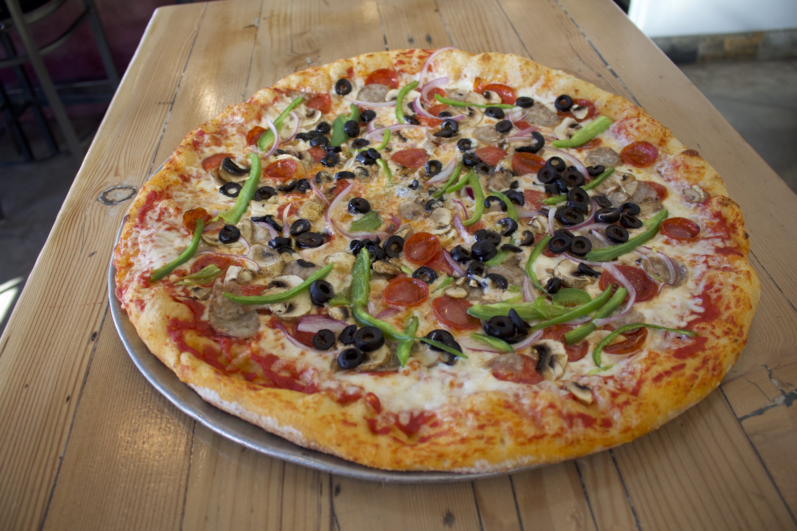 A loaded HomeSlice supreme-style pizza on a table, ready to share