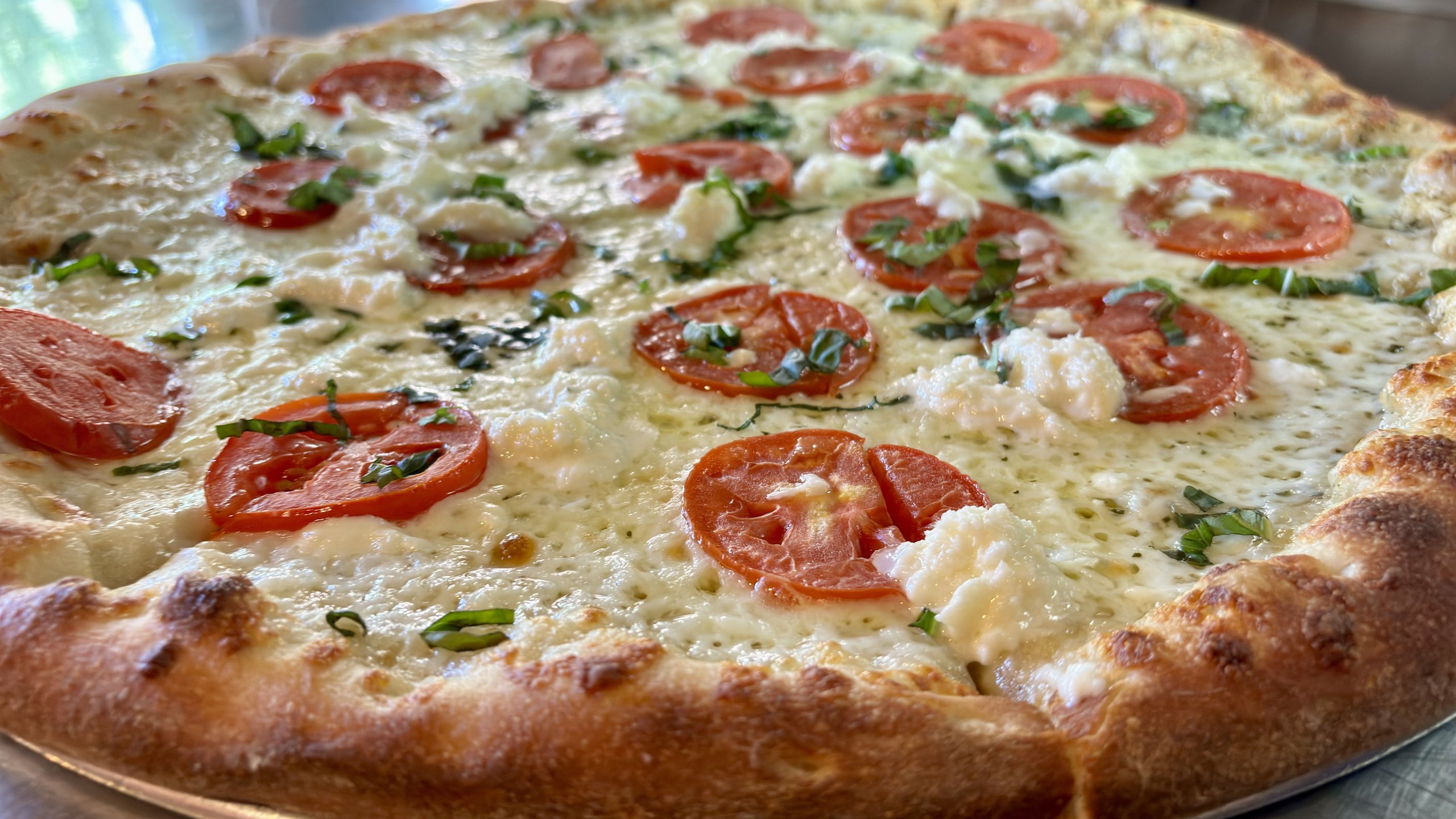 Angled shot of a white pizza topped with tomato and basil