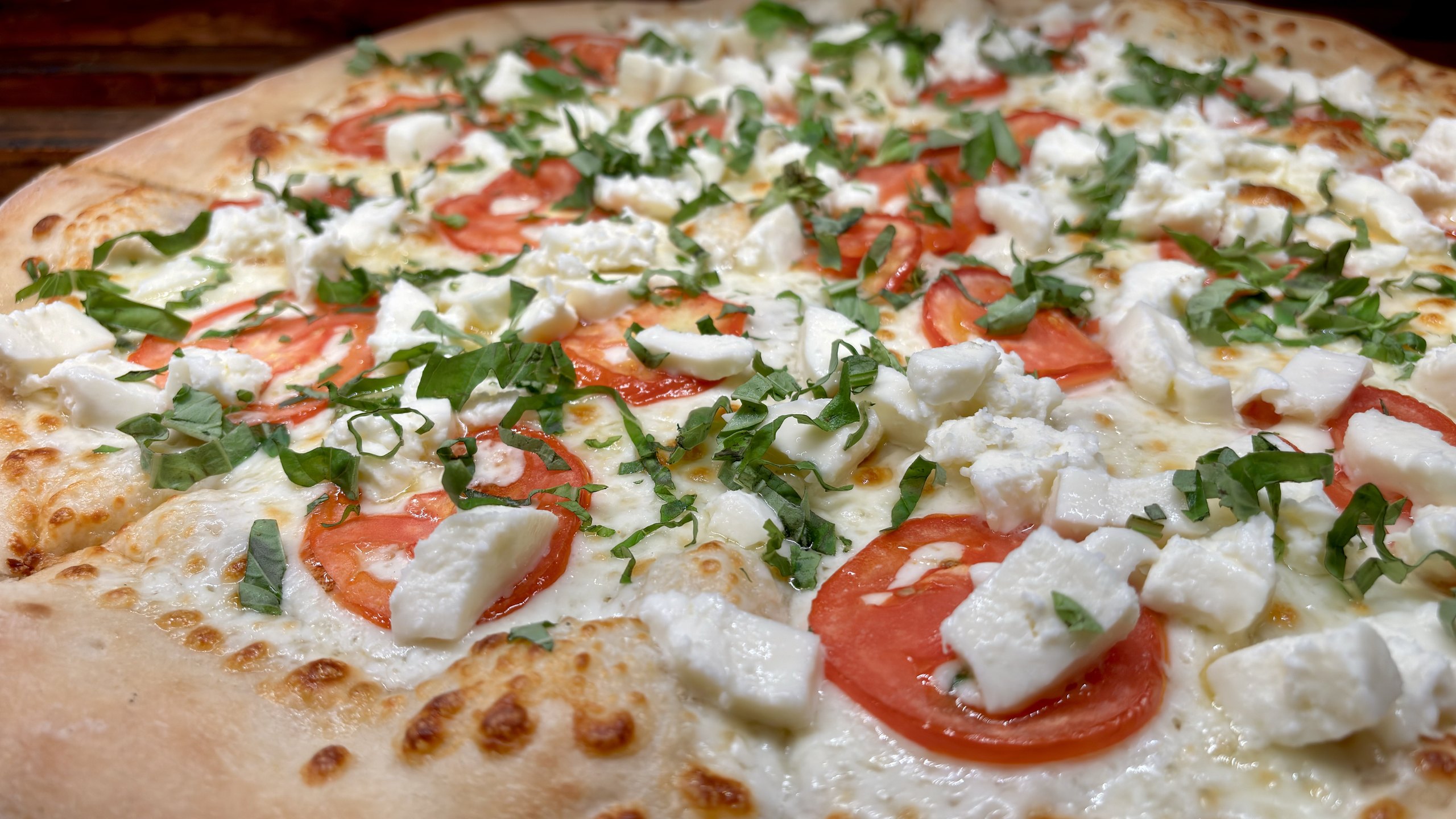 Macro close-up of a white pizza topped with tomato and basil
