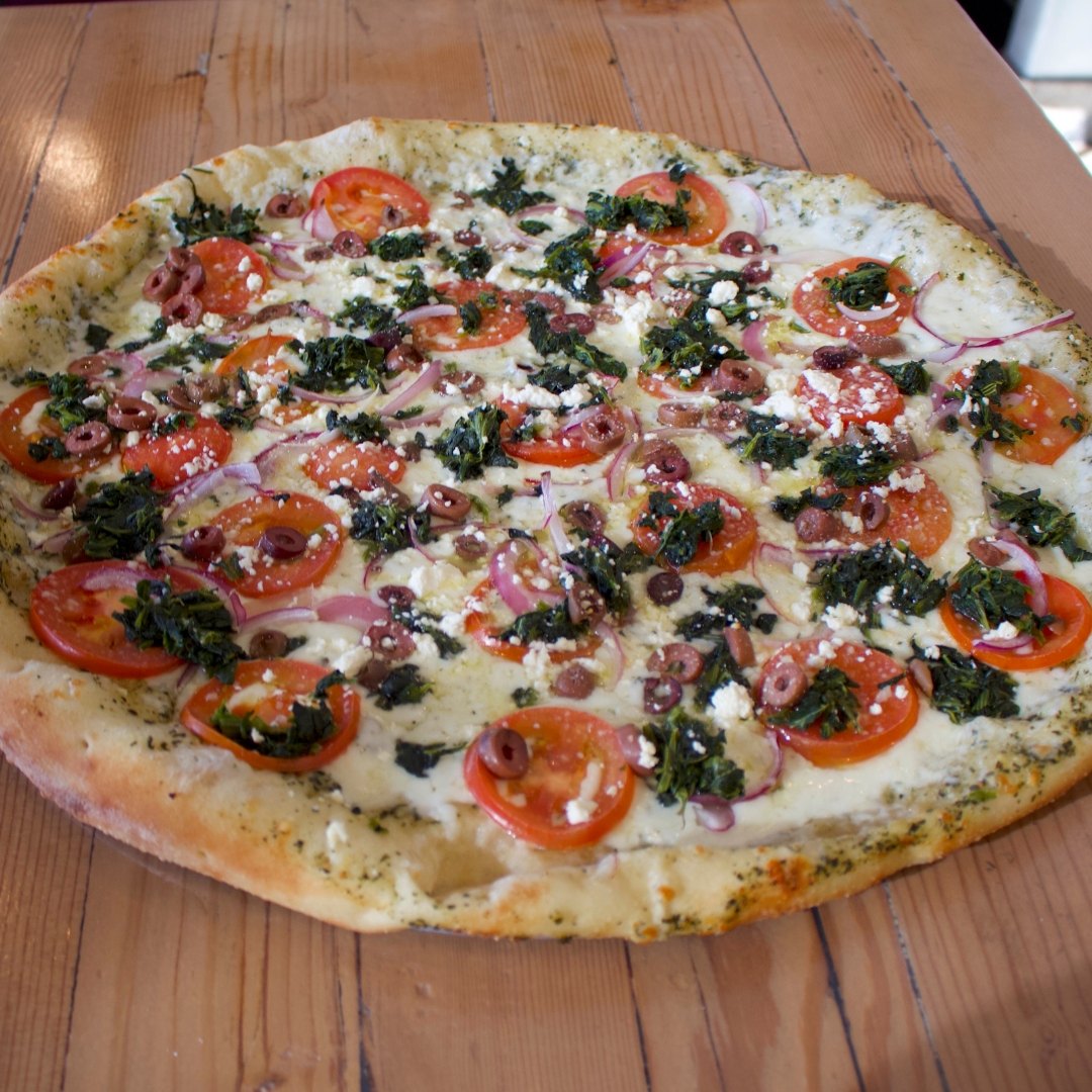 Overhead shot of a white pizza topped with spinach, tomato and red onion