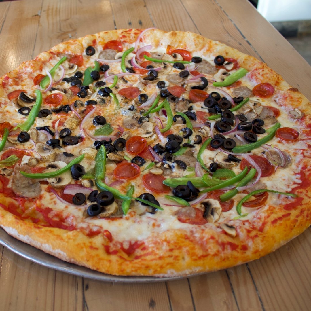 Overhead view of a HomeSlice pizza loaded with a mix of meat and vegetable toppings