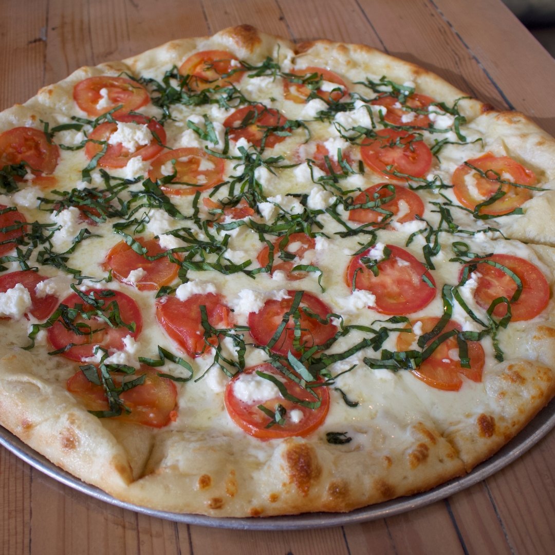 Overhead view of a white pizza topped with tomato, basil, and feta